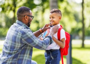 Father escorts happy first-grader boy to school, straightens his bow tie before classes