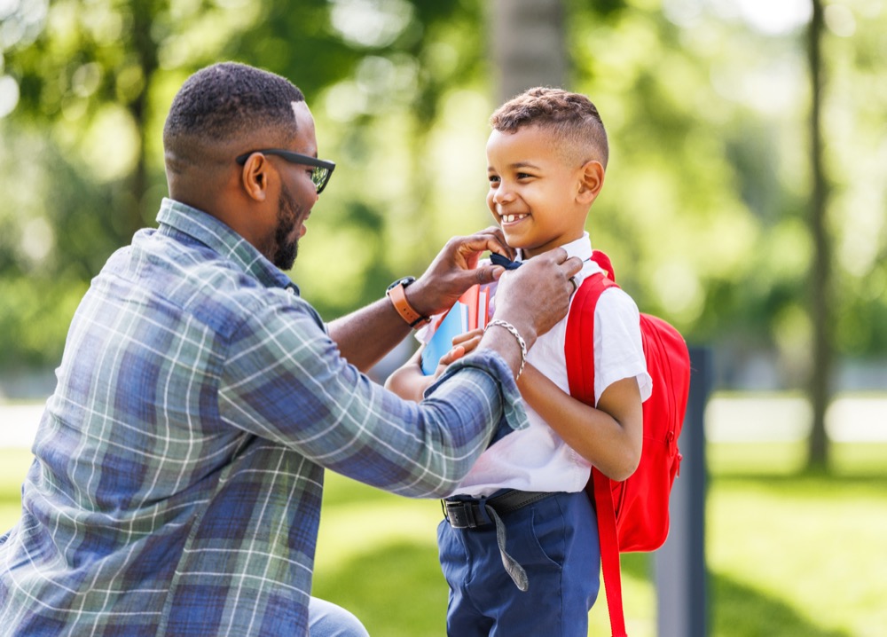 Father escorts happy first-grader boy to school, straightens his bow tie before classes