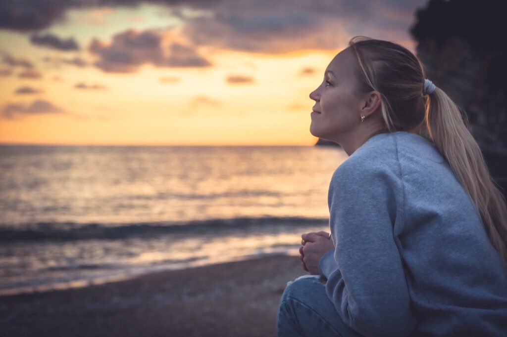 Pensive lonely smiling woman looking with hope into horizon during sunset at beach